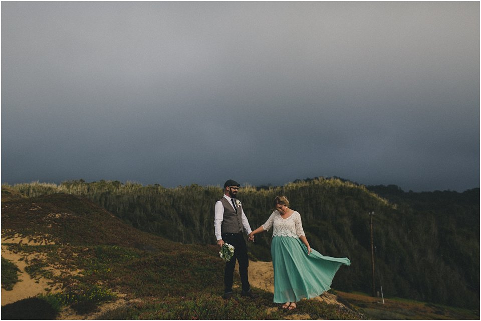 bride and groom stand on sand dune under overcast skies after they eloped