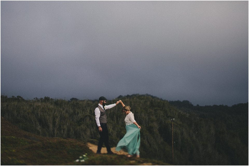 groom twirls bride on a sand dune with overcast skies above 