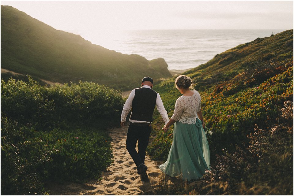 groom leads bride down a trail between two sand dunes after they eloped