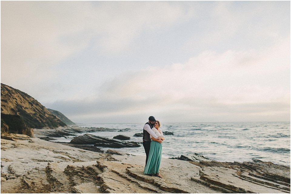 groom holds bride on a rock overlooking the ocean