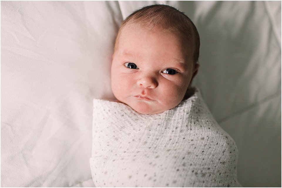 newborn baby wrapped in blanket looking at the camera